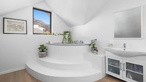 A modern bathroom with a freestanding bathtub, white cabinetry, and a large window offering a view of the outdoors. - Uptown Retreat (Cape Town)