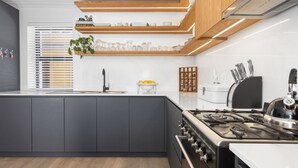A modern kitchen with grey cabinets, a stainless steel stove, and wooden shelves above the counter. - Uptown Retreat (Cape Town)