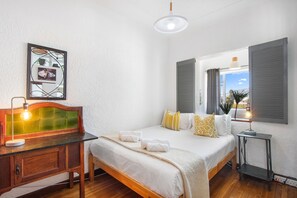 Un dormitorio con cama, mesita de noche, lámpara y vistas al exterior.
