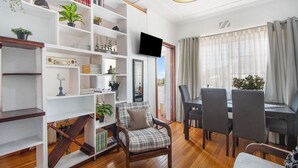 A living room with a wooden floor, a dining area with a table and chairs, and a bookshelf filled with books and plants. - Langholm 45 on Kloof (Cape Town)