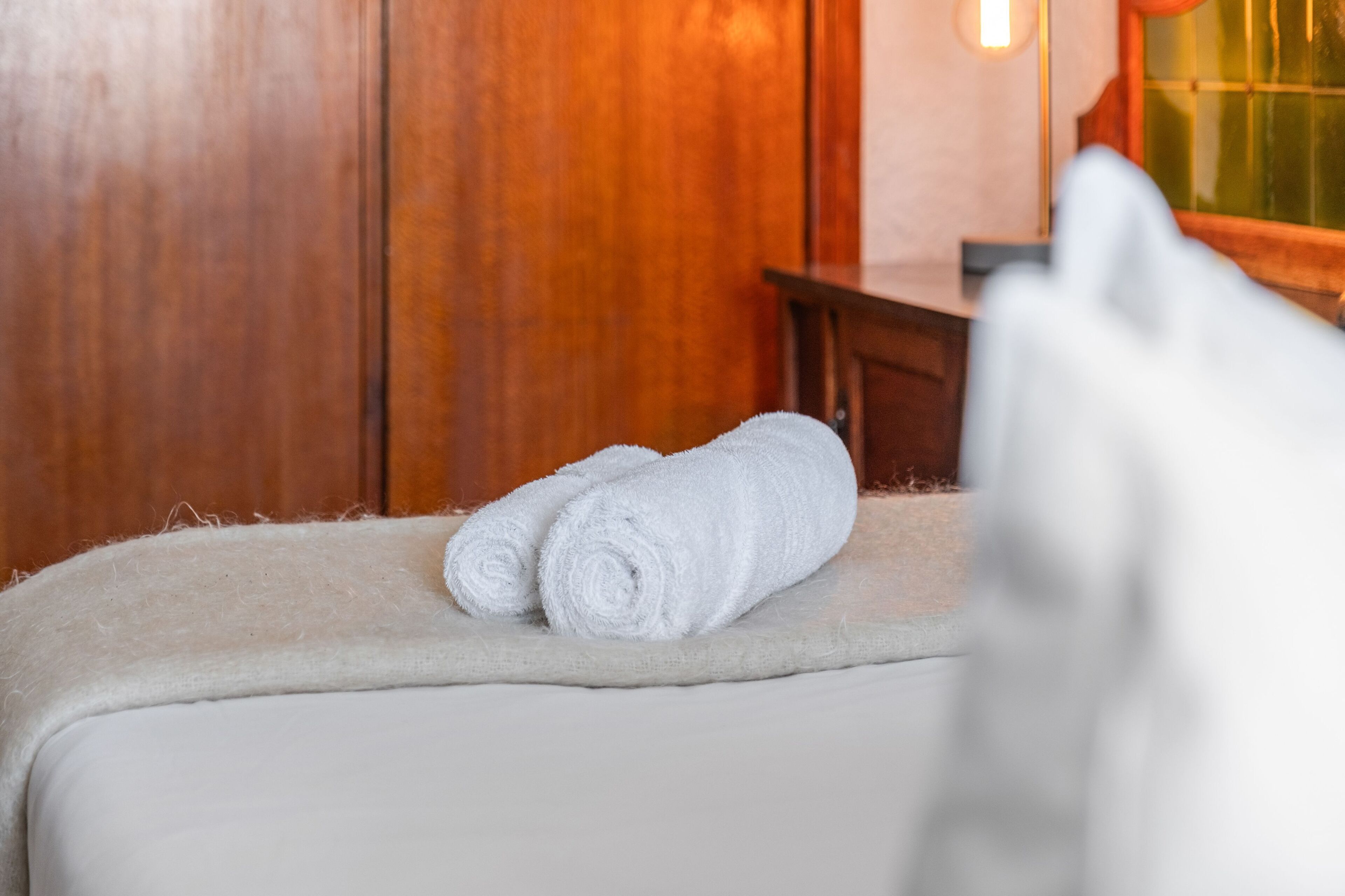 A neatly made bed with two rolled white towels and a fluffy white pillow.