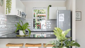 Una cocina moderna con armarios blancos, un refrigerador de acero inoxidable, una ventana con vista a un parque infantil y una planta en maceta sobre la encimera.