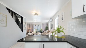 Una cocina moderna con encimera negra, armarios blancos y una escalera que conduce a una sala de estar.