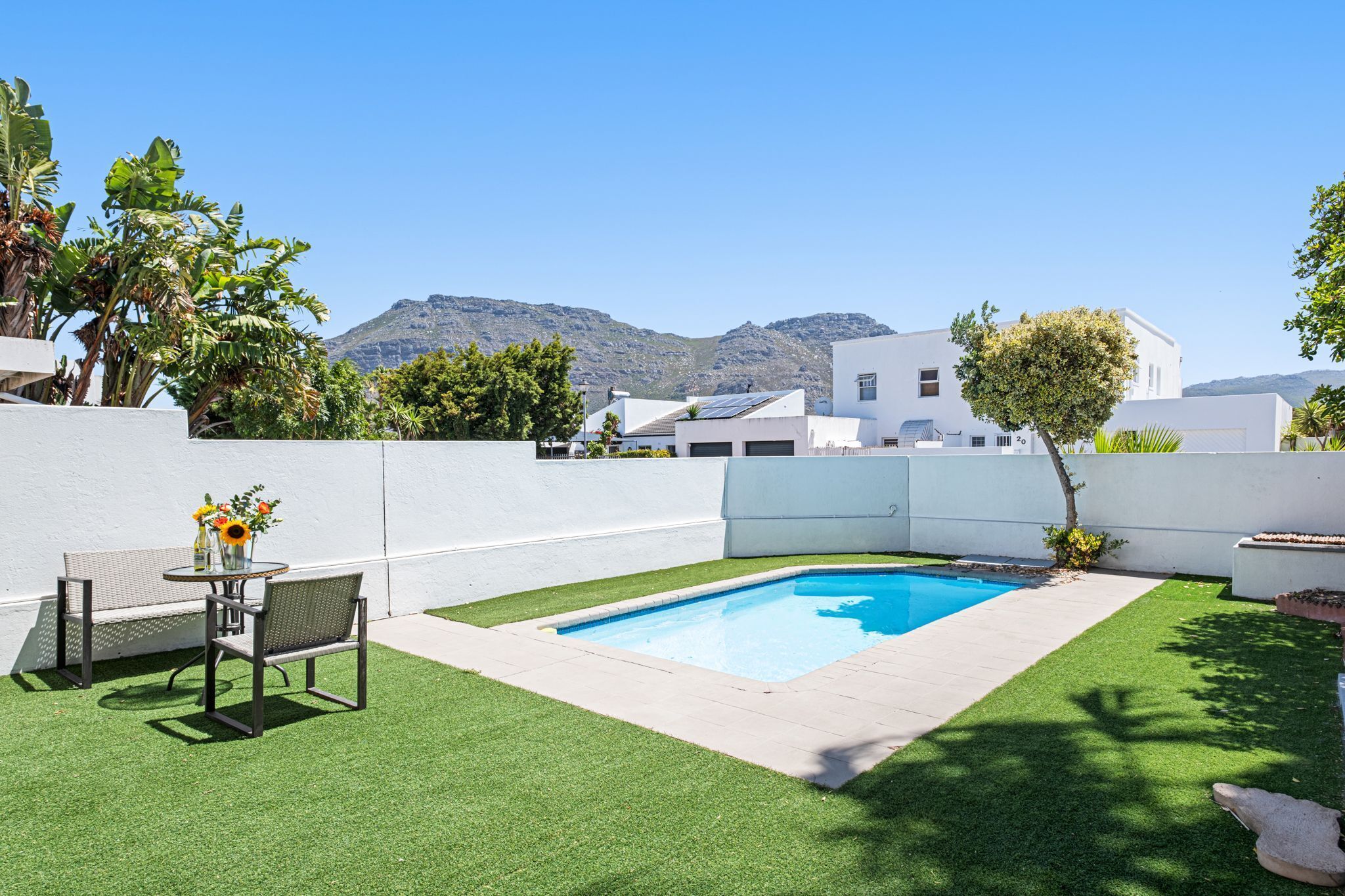 A pool area with artificial grass, a table with chairs, and a mountain view in the background.