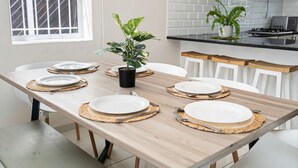 Una mesa de comedor dispuesta con platos, cubiertos y manteles individuales en una cocina moderna con armarios blancos y una planta en maceta.