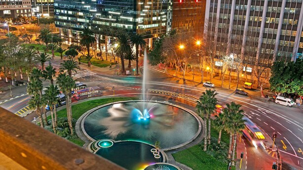 A city intersection with a roundabout, palm trees, and modern buildings. - Fountain Suites 1102 (Cape Town)