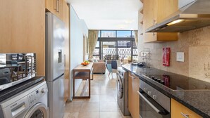 A modern kitchen with stainless steel appliances, a washing machine, and a dining area with a view of the city. - Fountain Suites 1102 (Cape Town)