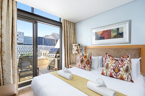 A hotel room with a large bed, a view of the cityscape, and a balcony with outdoor furniture. - Fountain Suites 1102 (Cape Town)