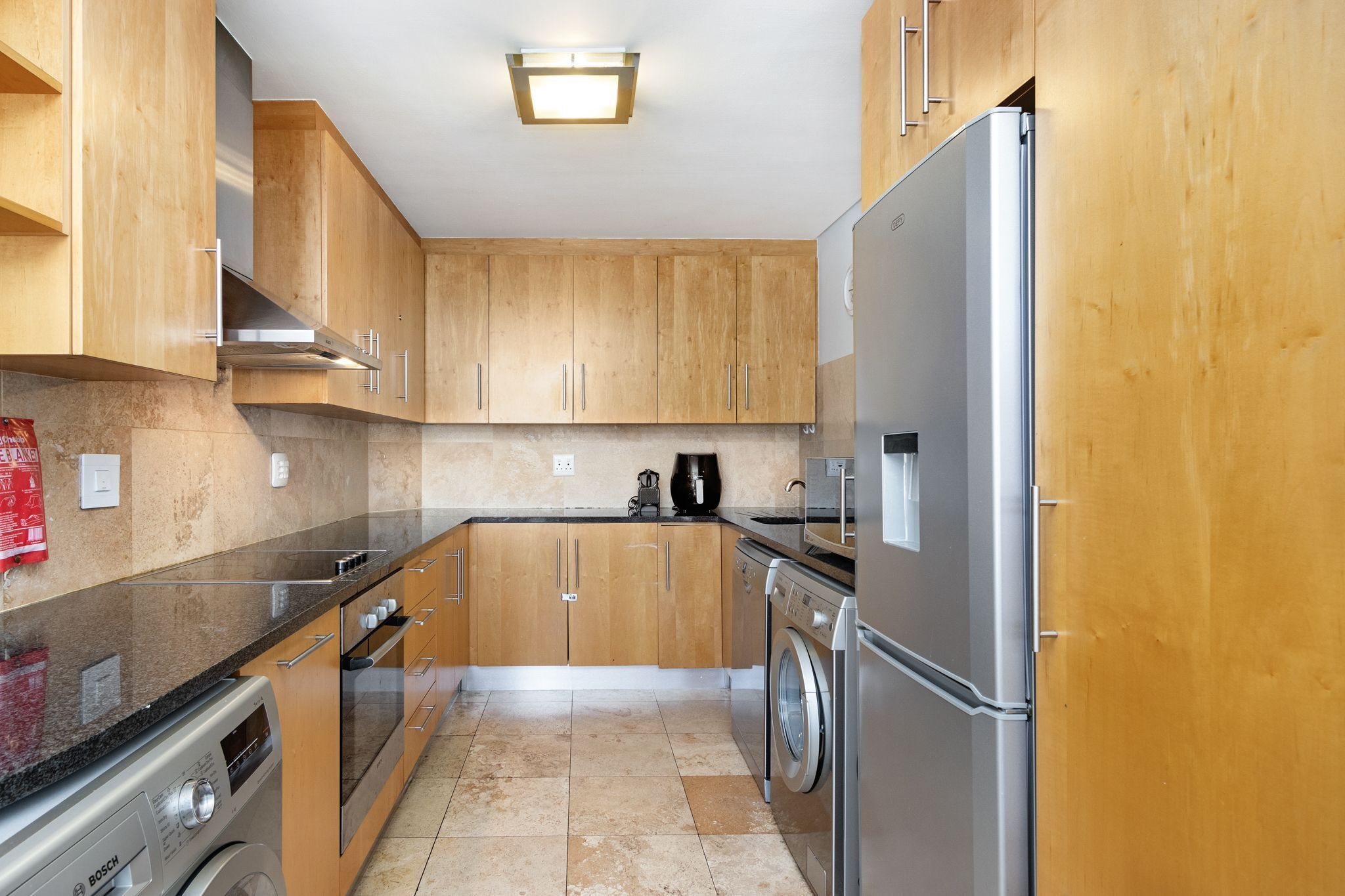 Une cuisine compacte avec des meubles en bois, des appareils en acier inoxydable et un lave-linge.