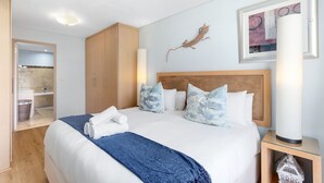 A hotel room with a large bed, a wooden wardrobe, a bathroom visible through an open door, and a wall-mounted artwork. - Fountain Suites 1102 (Cape Town)