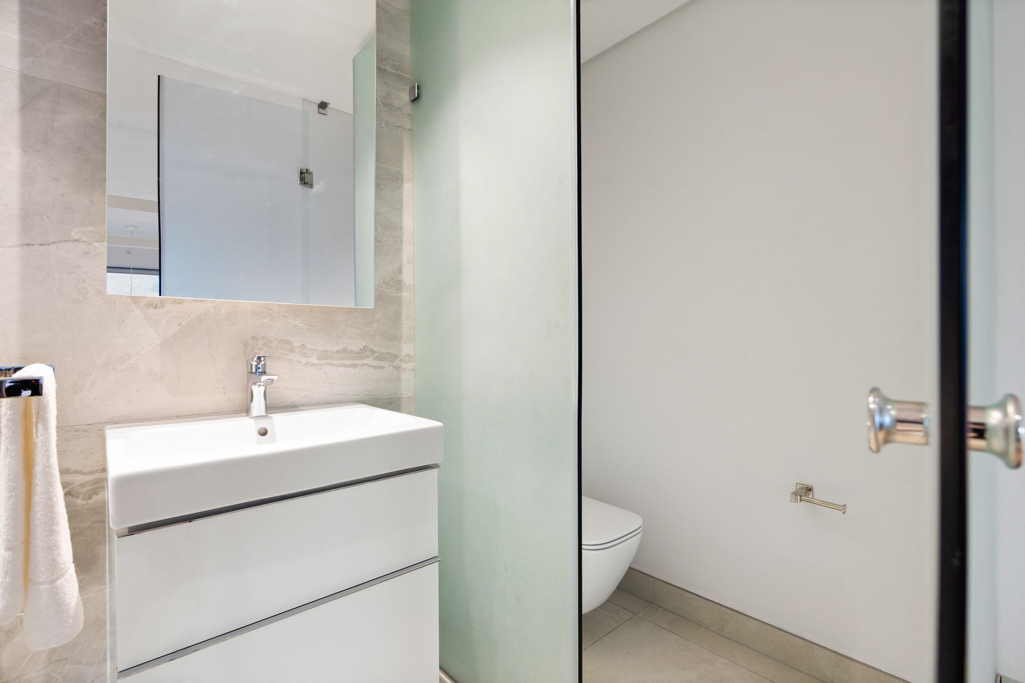 A modern bathroom with a white sink, a glass shower enclosure, and a toilet.