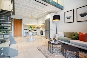 A modern living space with a staircase, a dining area, a kitchen, and a sofa with cushions. - Apartment 307 at 117 on Strand (Cape Town)