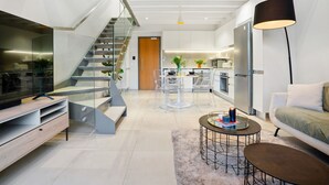 Uma cozinha moderna com uma ilha central, área de jantar com cadeiras transparentes e escada que leva a um andar superior.