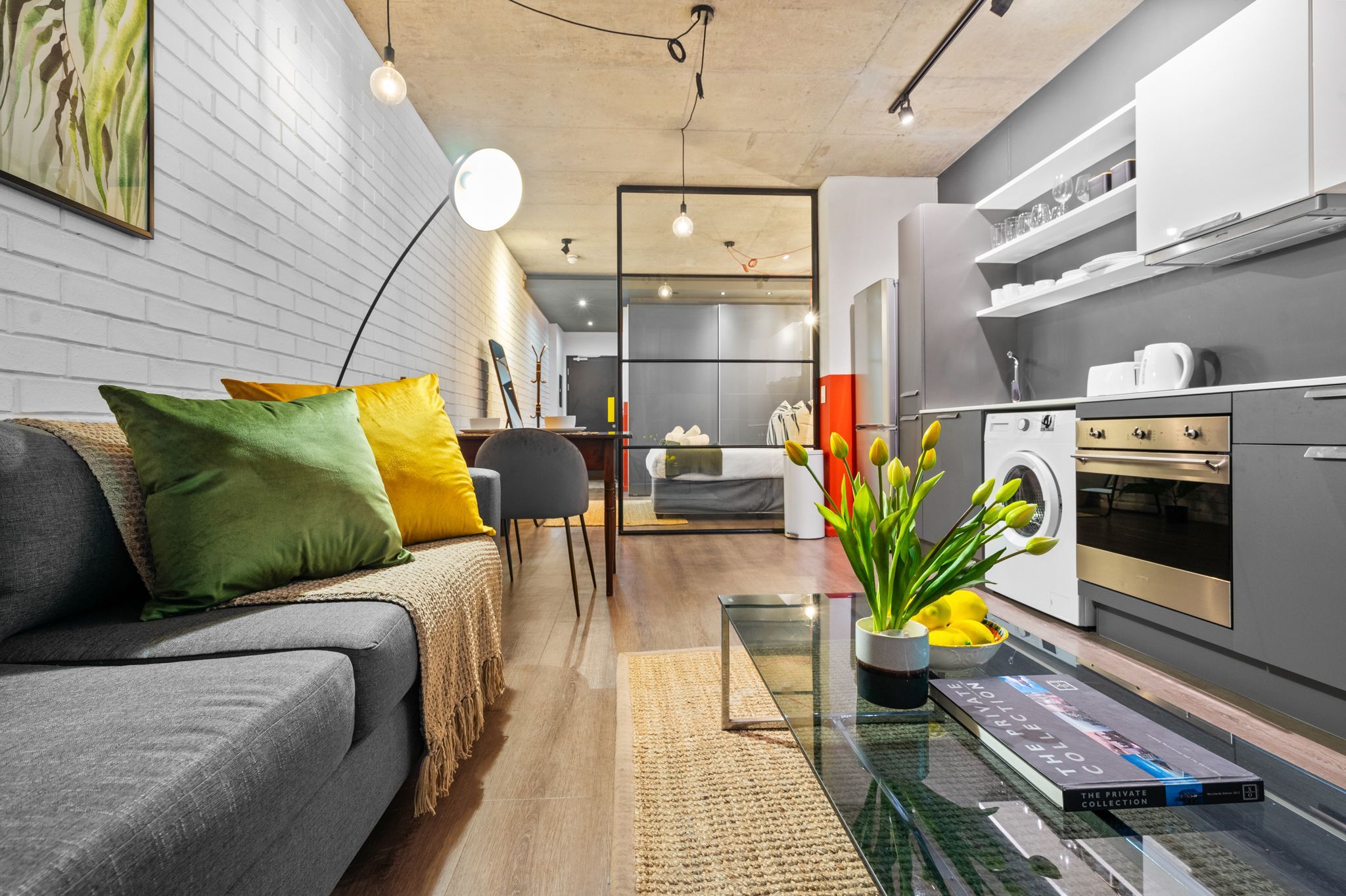 A modern living room with a grey sofa, colorful cushions, a glass coffee table, and a potted plant.