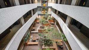 Un amplio atrio interior con una cubierta de madera central, rodeado de zonas de estar y macetas, que presenta un diseño arquitectónico moderno con paredes de ladrillo visto y un nivel entre pisos.