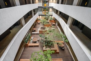 A spacious indoor atrium with a central wooden deck, surrounded by seating areas and planters, featuring a modern architectural design with exposed brick walls and a mezzanine level. - The Wex 620 (Cape Town)