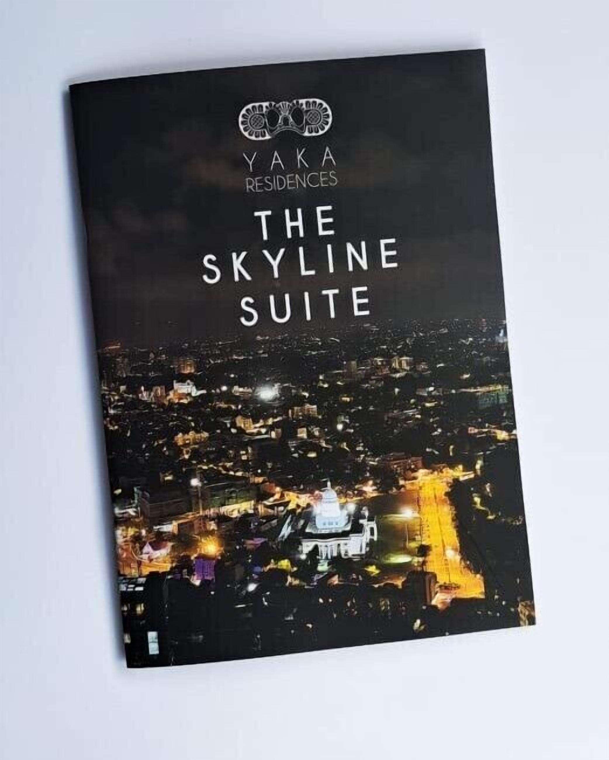 Portada de un folleto de Yaka Residences. La Suite Skyline, con una vista nocturna de la ciudad que muestra edificios iluminados y una estructura blanca destacada.
