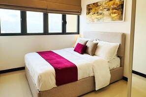 A neatly made bed with a white and red bedspread, a beige headboard, and a painting on the wall. - YAKA Trizen Luxury Apartments (Colombo)