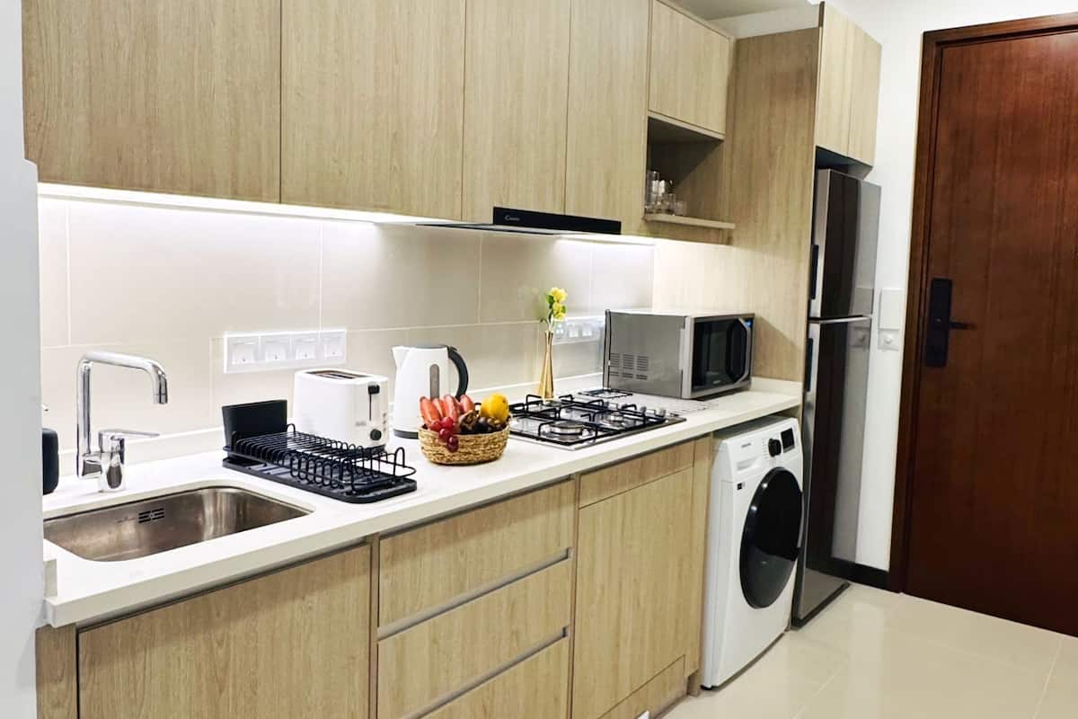 A modern kitchen with wooden cabinets, a stainless steel sink, a microwave, a gas stove, and a built-in washing machine.