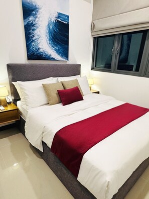 A neatly made bed with white and red bedding, a grey headboard, and a red throw blanket. - YAKA Trizen Luxury Apartments (Colombo)