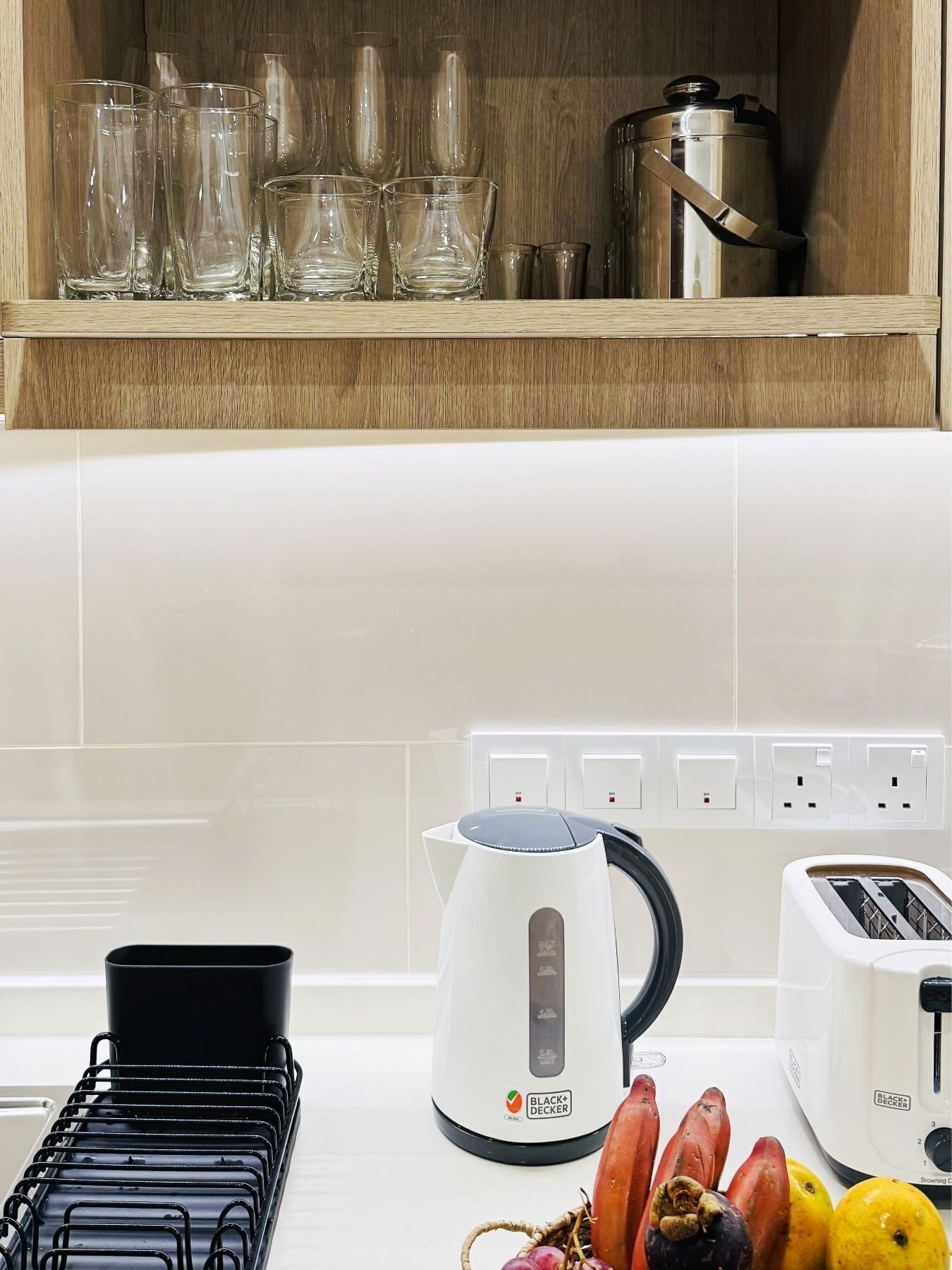 Una cocina con hervidor, tostadora y un expositor de tazas negras.
