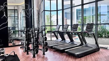 A modern gym with treadmills, weight machines, and a large window offering a view of the city.