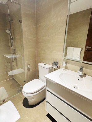 A modern bathroom with a glass-enclosed shower, a toilet, a sink, and a mirror. - YAKA Trizen Luxury Apartments (Colombo)