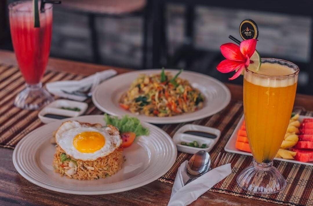 A table with two plates of fried rice, one with a fried egg, and a glass of orange juice.