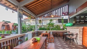 Un área de estar al aire libre con mesas y bancos de madera, una barra con el rótulo de Heineken, y vistas de edificios y vegetación circundante.