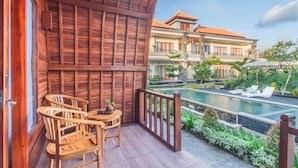 A wooden balcony with a pool and lounge chairs, overlooking a landscaped garden and a building with a tiled roof. - MAILAKU HOUSE (Kerobokan Kaja)