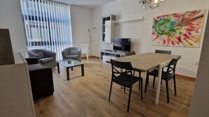 A modern living room with a sofa, coffee table, and dining table with chairs. There is a TV and a painting on the wall. - Centrally located in Sliema, this apartment puts you steps from shops, restaurants, cafés, and the lively promenade (Tas-Sliema)