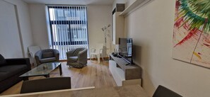 Ein modernes Wohnzimmer mit einer Couch, Sesseln, einem Couchtisch, einem Fernseher und einem Gemälde an der Wand.