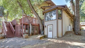 A rustic cabin with a wooden deck, a staircase, and a large window overlooking a wooded area. - Wfh-friendly Retreat < 1 Mi to Clear Lake! (Kelseyville)