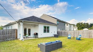 Ein Haus mit überdachter Terrasse, Grill und umzäunter Garten.