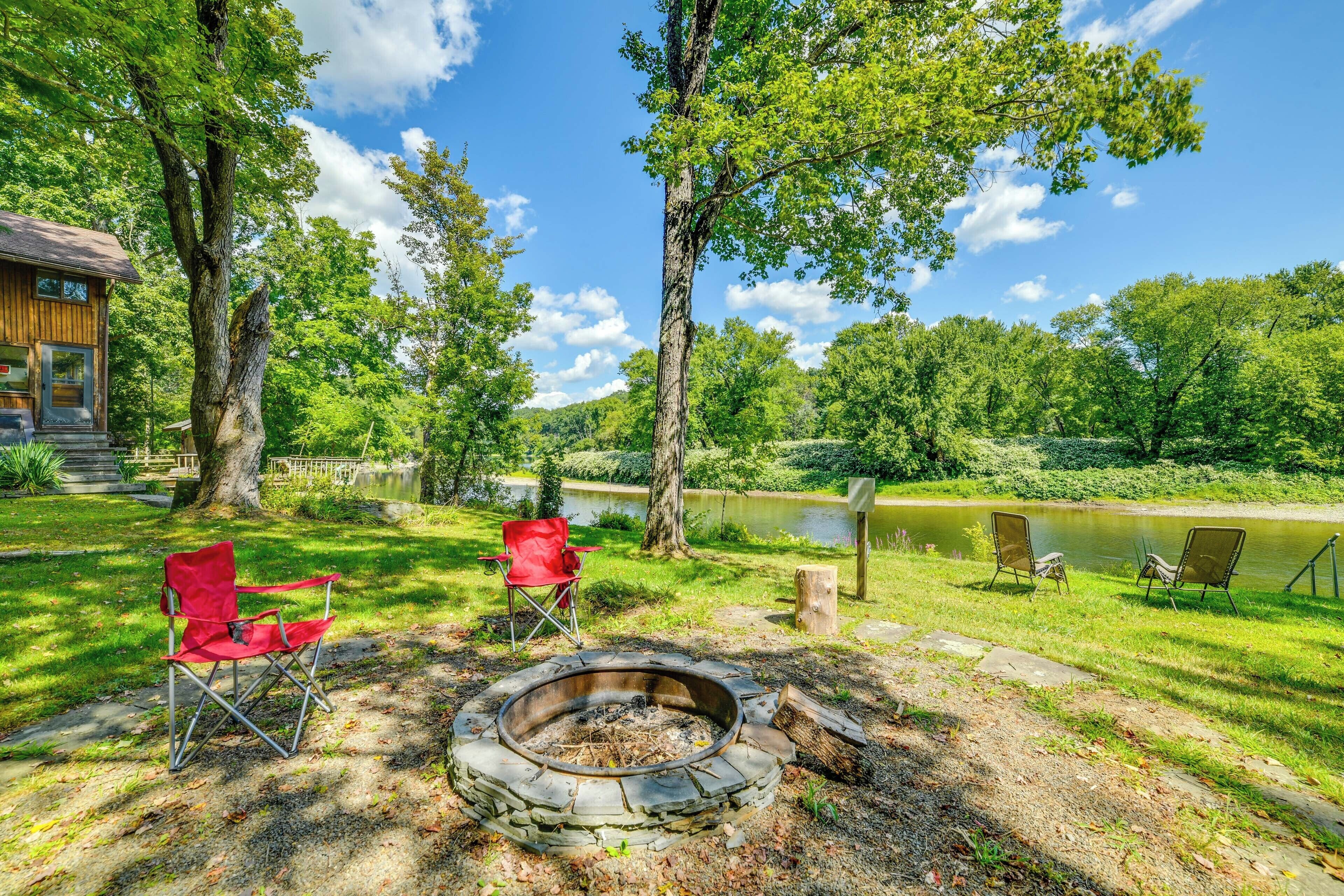 A campsite with a fire pit, red chairs, and a view of a lake.