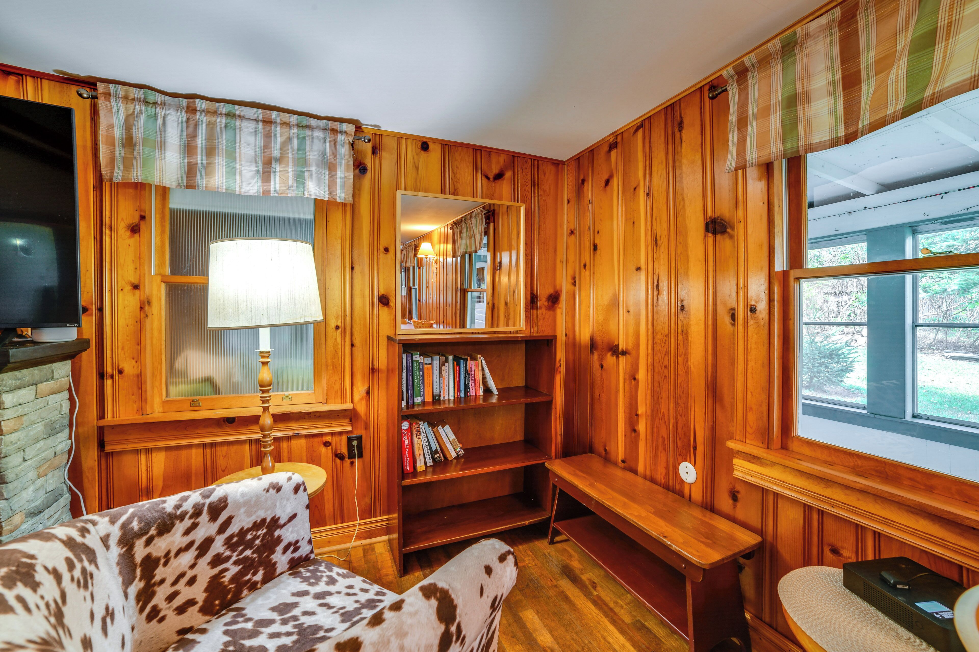 Une pièce chaleureuse avec des murs en bois, un canapé, une bibliothèque, une lampe et un téléviseur.