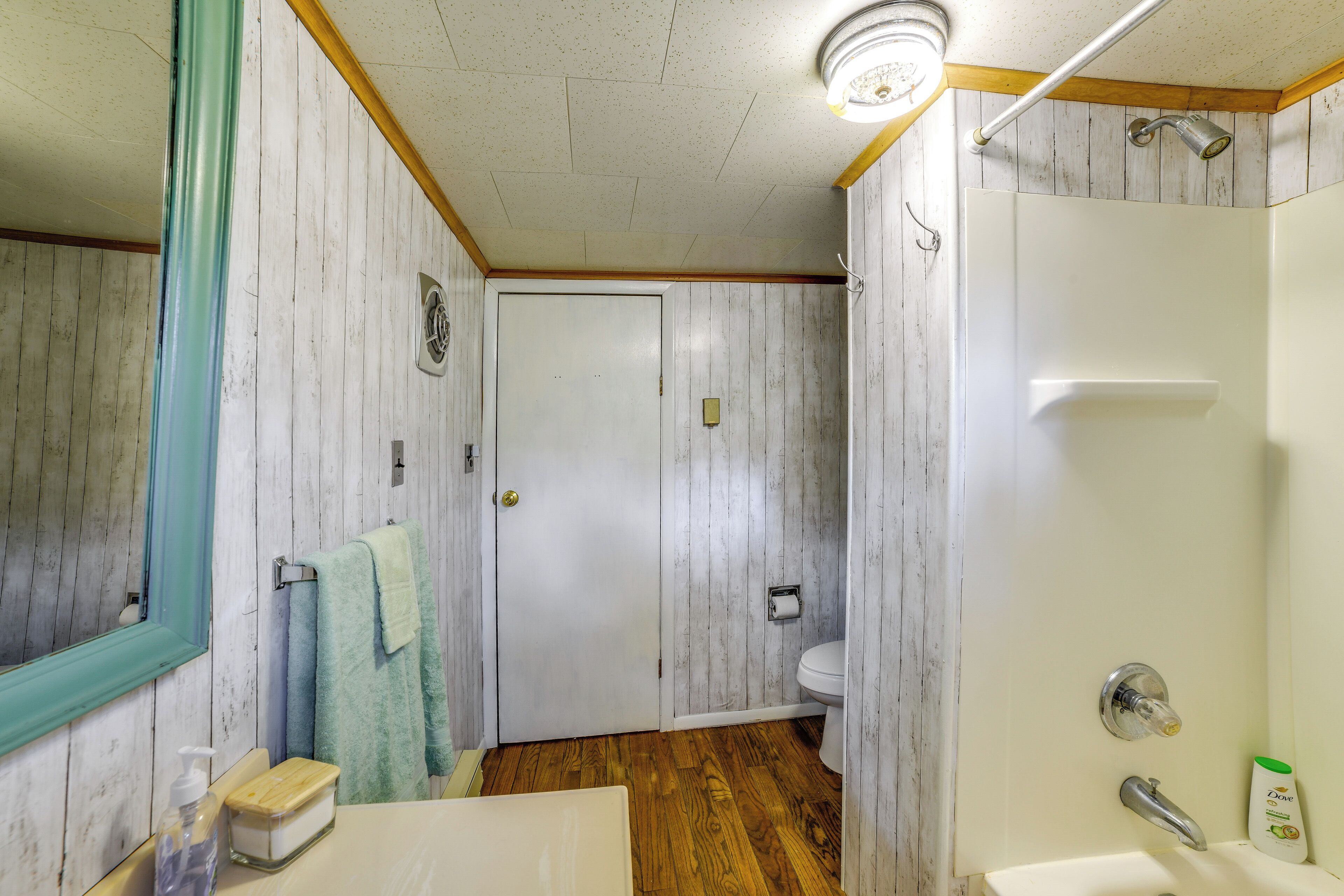 A bathroom with a wooden floor, a white sink, a mirror, and a shower area.