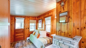 Un dormitorio de cabaña de madera con chimenea de piedra, una cama con almohadas y una ventana con persianas.