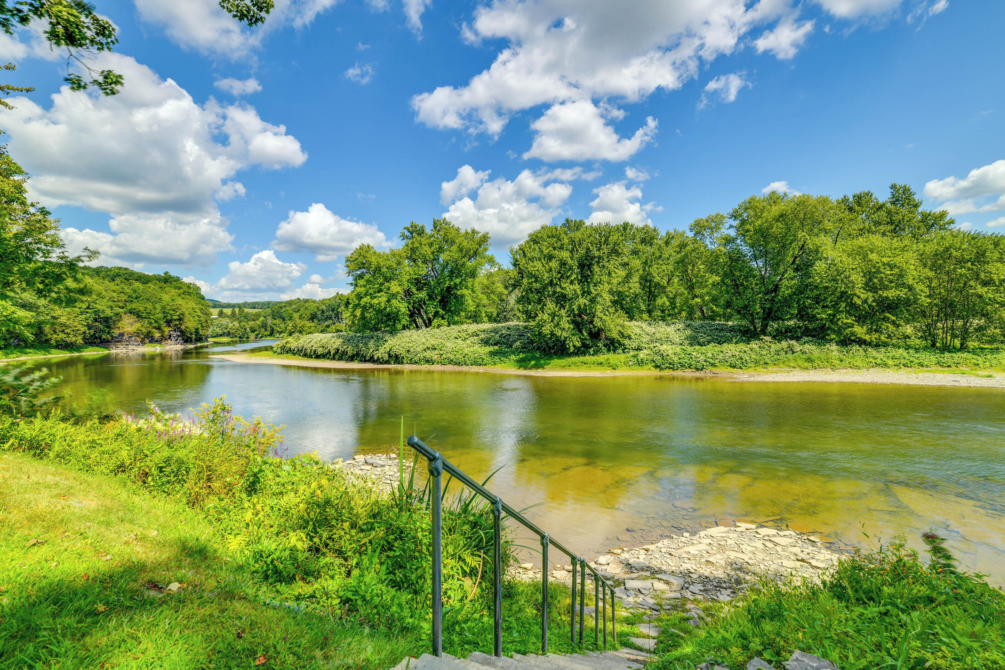 A river with a stone staircase leading down to the water, surrounded by lush greenery and trees.
