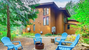 Eine Holzhütte mit Feuerstelle und blauen Adirondack-Stühlen im Garten.