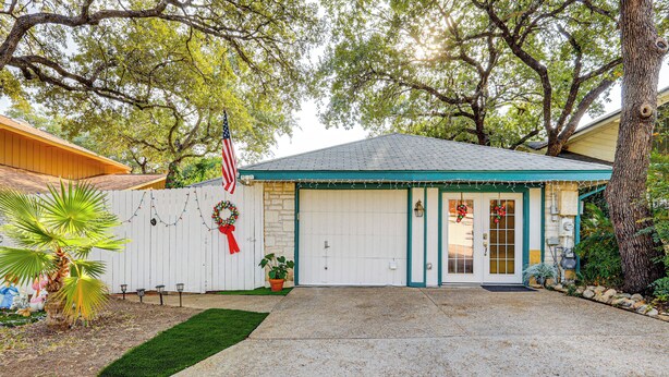 A house with a white garage door, a front porch, and a small garden with a palm tree. - Private Yard w/ Pool: Quiet Getaway in San Antonio (San Antonio)