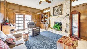 A spacious living room with a fireplace, a ceiling fan, wooden paneling, and a large bookshelf. - Private Yard w/ Pool: Quiet Getaway in San Antonio (San Antonio)