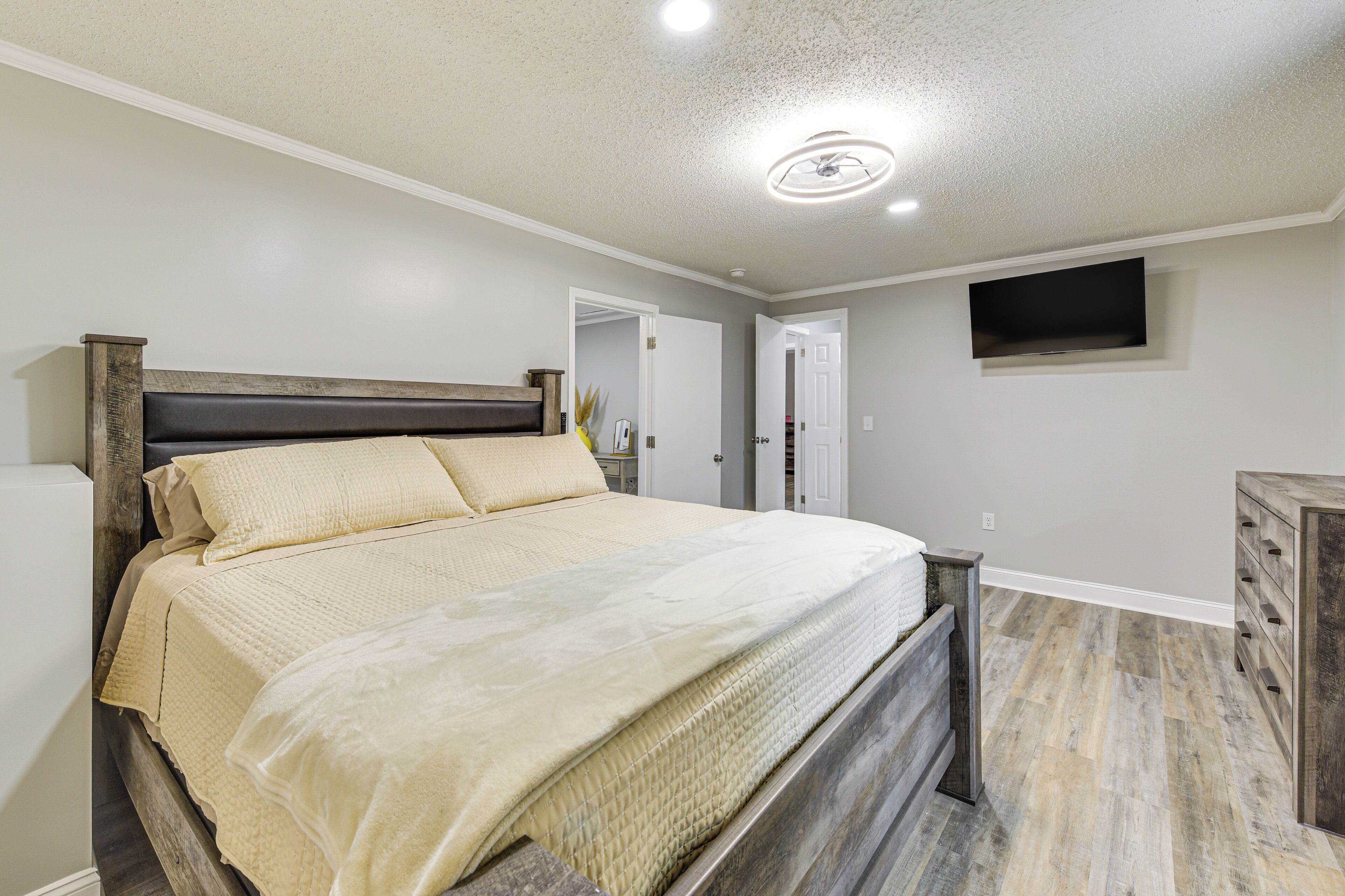 A bedroom with a bed, a dresser, a ceiling fan, and a TV mounted on the wall.