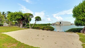 Une zone sablonne avec une étendue d’eau, entourée de verdure et d’un bâtiment doté d’un toit plat.
