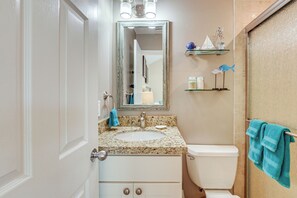 Une salle de bain avec un lavabo, des toilettes et un miroir. Des serviettes sont accrochées au mur, et une étagère contient des articles de toilette.