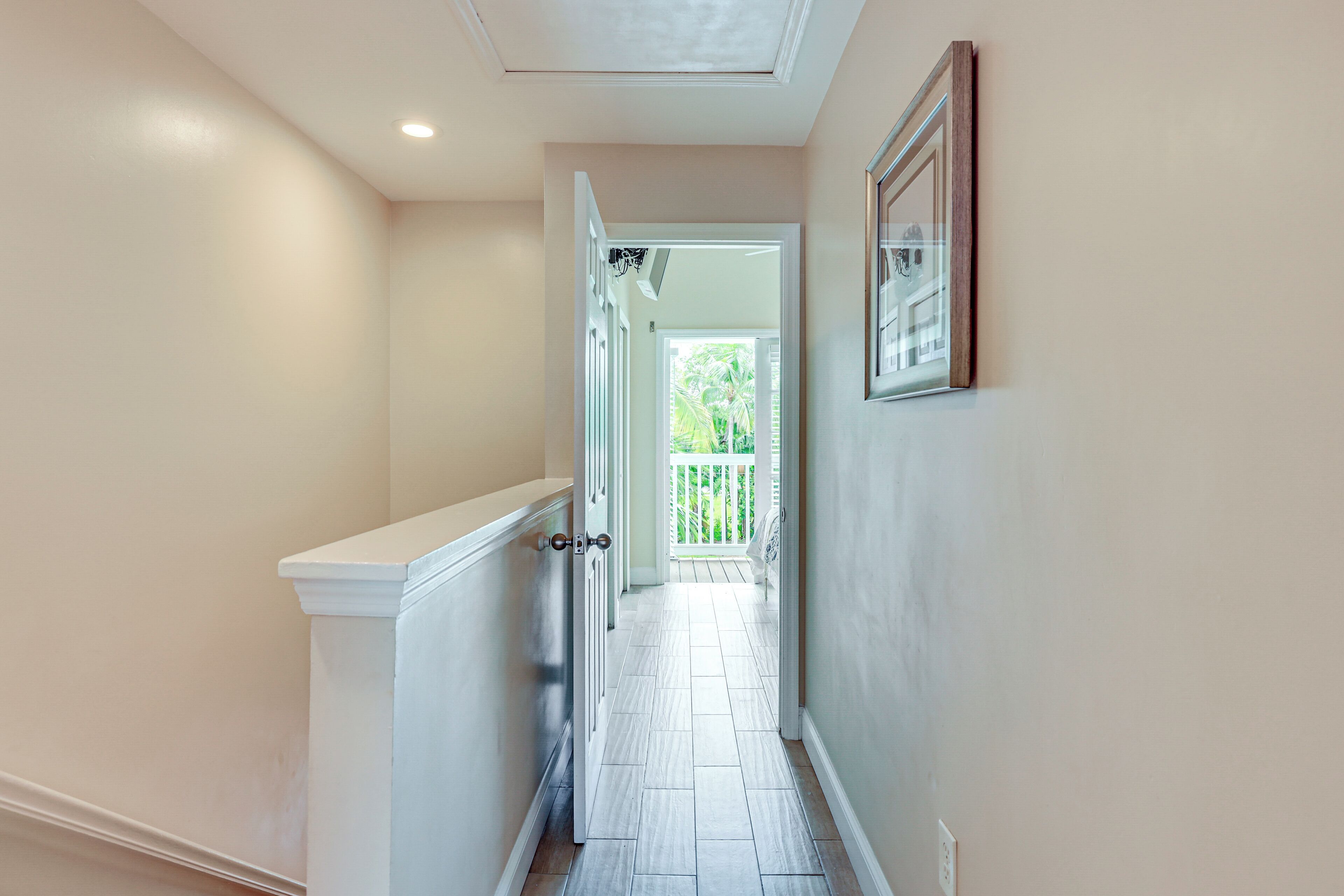 A narrow hallway with white walls and a white baseboard, leading to a balcony with a white railing.