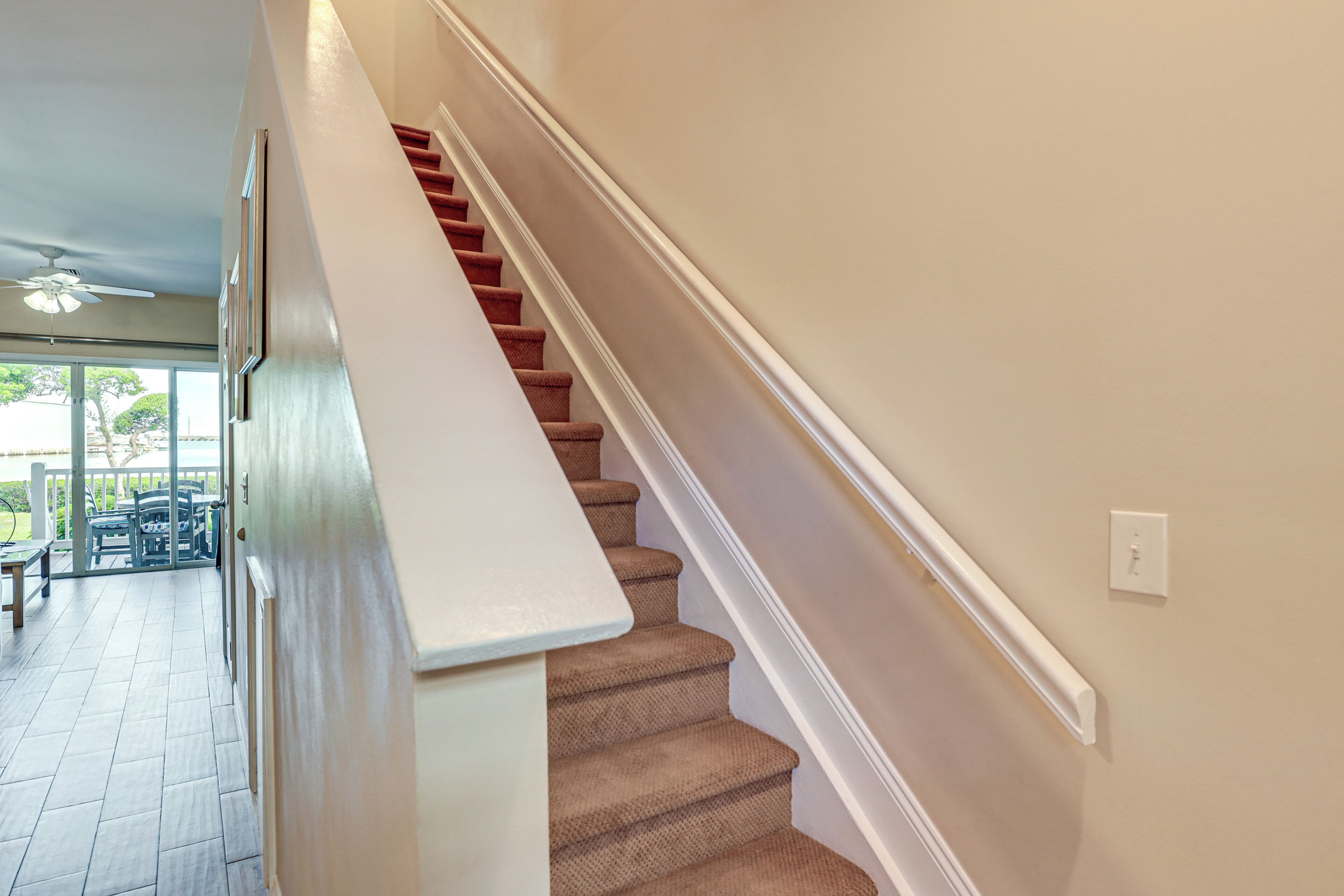 A staircase with a beige carpet and white handrail, leading to a room with a white ceiling and a ceiling fan.