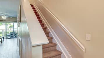 A staircase with a beige carpet and white handrail, leading to a room with a white ceiling and a ceiling fan.