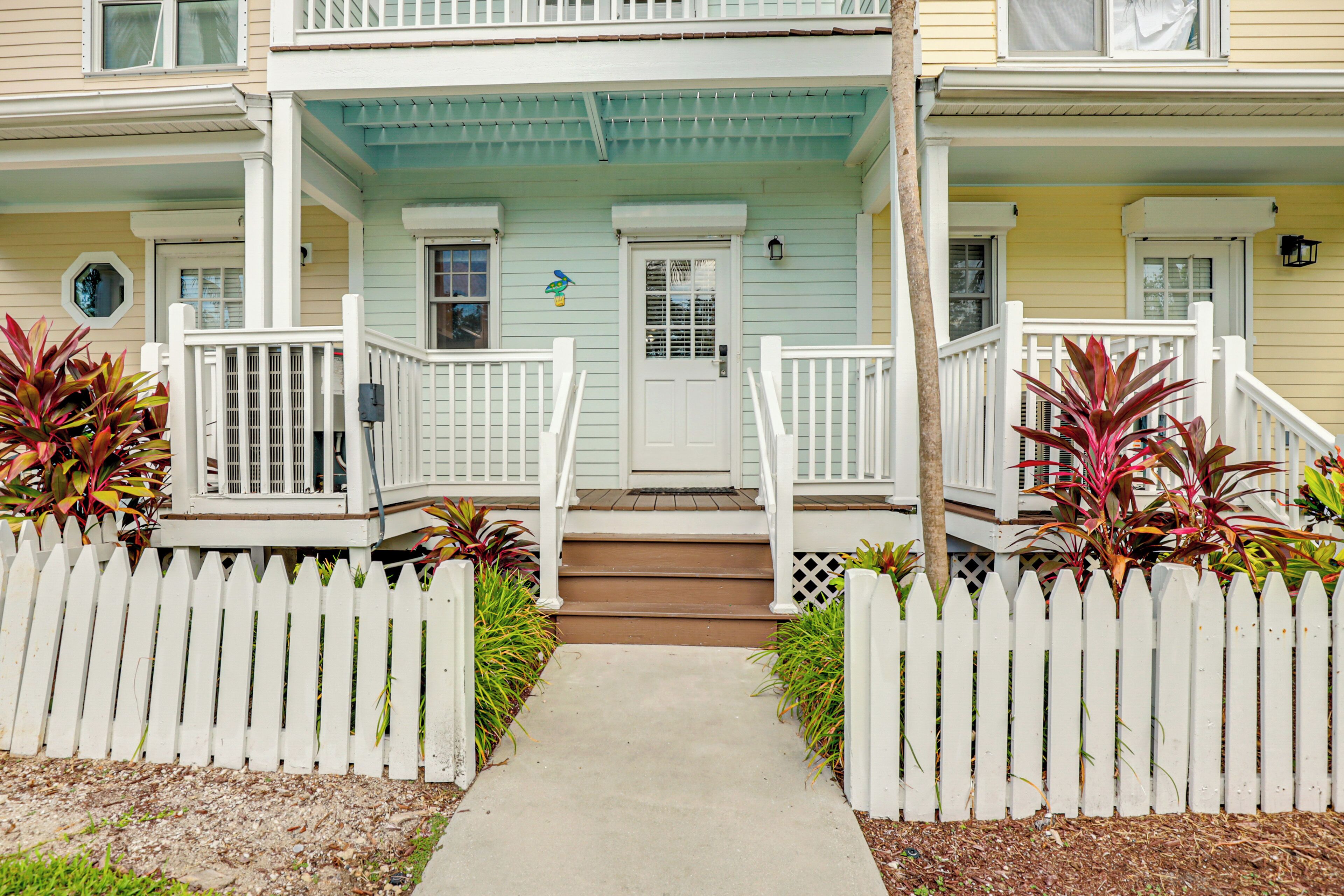 A two-story house with a front porch, white picket fence, and steps leading to the door.