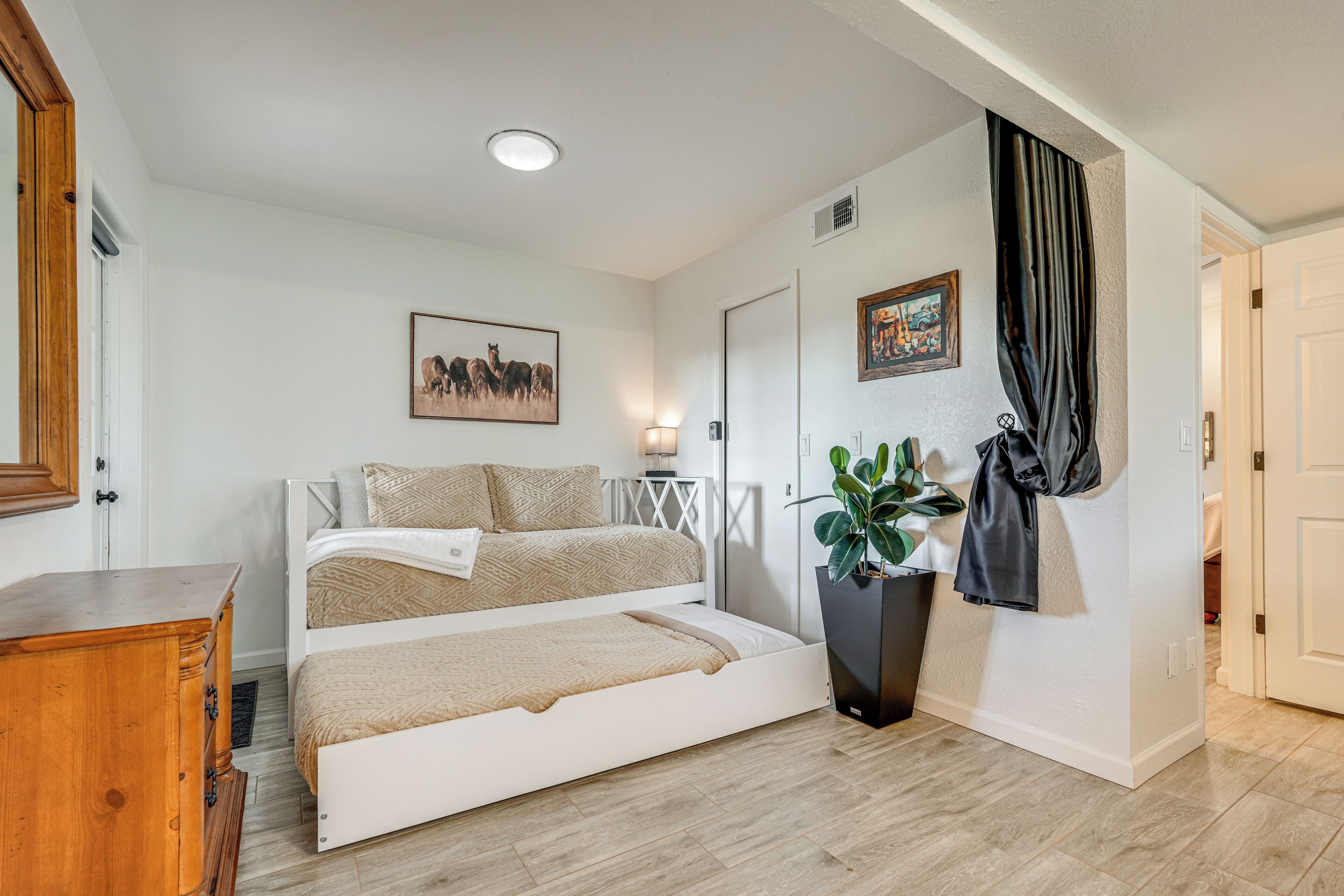 A bedroom with a bed, a dresser, a plant, and a painting on the wall.
